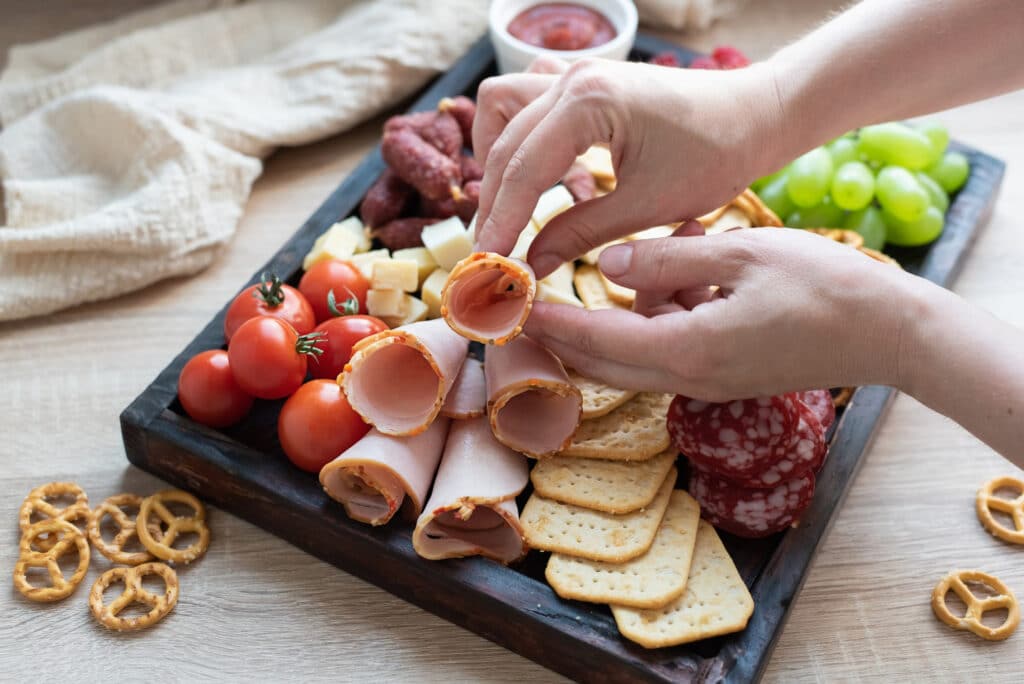 Femme préparant un plateau apéritif avec des produits à partager.