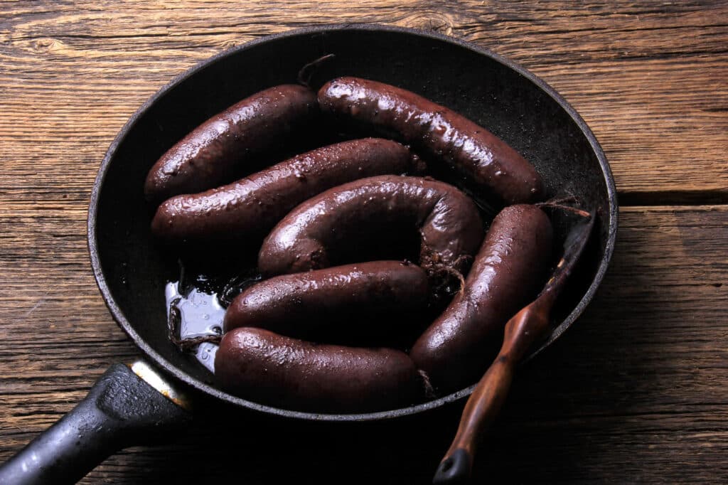 Cast‑iron skillet filled with glossy cooked sausages soaking in oil on a rustic wooden table
